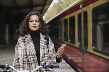 Woman with bicycle and cell phone on an underground station platform, Berlin, Germany - AHSF01198