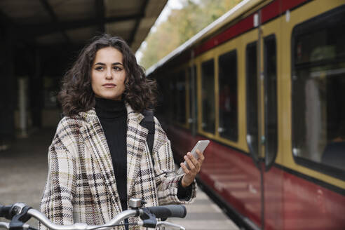 Frau mit Fahrrad und Mobiltelefon auf dem Bahnsteig einer U-Bahn-Station, Berlin, Deutschland - AHSF01198