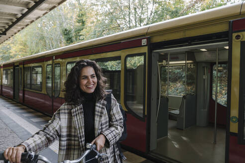 Glückliche Frau mit Fahrrad auf einem U-Bahn-Bahnsteig, Berlin, Deutschland - AHSF01200