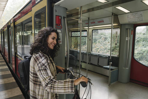 Smiling woman with bicycle entering an underground train, Berlin, Germany - AHSF01201