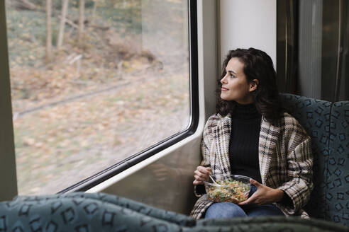 Young woman having lunch on a subway looking out of window - AHSF01211