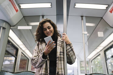 Smiling young woman using smartphone on a subway - AHSF01215