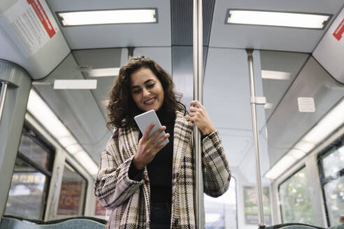 Lächelnde junge Frau mit Smartphone in einer U-Bahn - AHSF01215