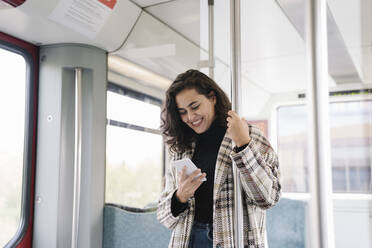 Lächelnde junge Frau mit Smartphone in einer U-Bahn - AHSF01217