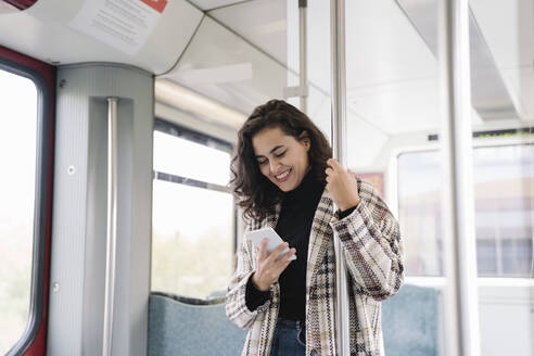 Lächelnde junge Frau mit Smartphone in einer U-Bahn - AHSF01217