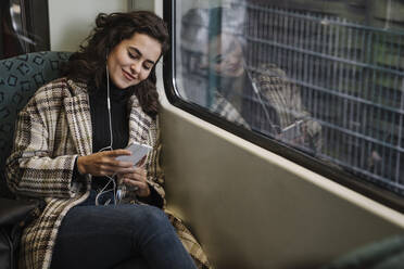 Junge Frau mit Kopfhörern und Smartphone in einer U-Bahn - AHSF01219