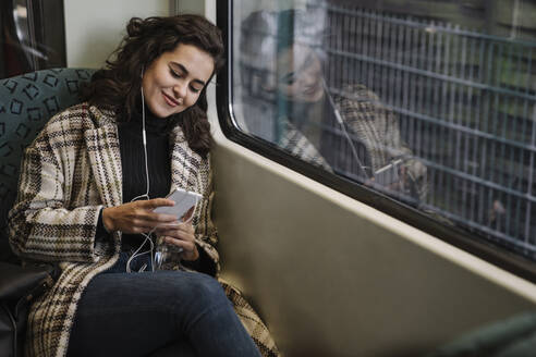 Young woman with earphones using smartphone on a subway - AHSF01219