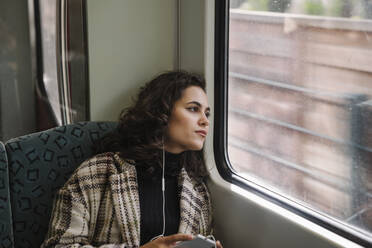 Junge Frau mit Kopfhörern in einer U-Bahn, die aus dem Fenster schaut - AHSF01220