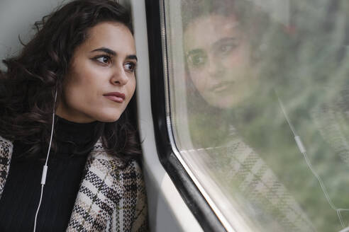 Junge Frau mit Kopfhörern in einer U-Bahn, die aus dem Fenster schaut - AHSF01221