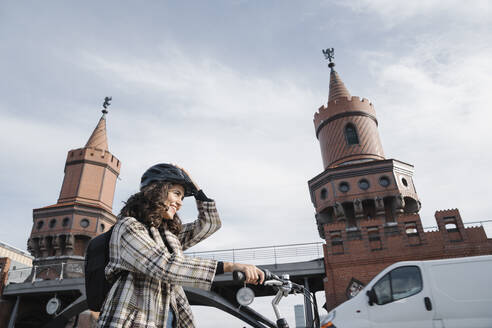 Lächelnde Frau mit einem Fahrrad in der Stadt an der Oberbaumbrücke, Berlin, Deutschland - AHSF01231