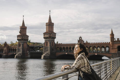 Lächelnde Frau mit Smartphone in der Stadt an der Oberbaumbrücke, Berlin, Deutschland - AHSF01238