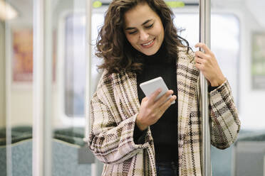 Smiling young woman using smartphone on a subway - AHSF01248