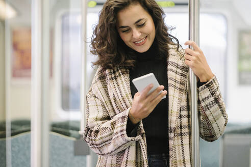 Lächelnde junge Frau mit Smartphone in einer U-Bahn - AHSF01248