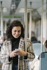 Smiling young woman using smartphone on a subway - AHSF01250