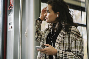 Junge Frau mit Kopfhörern und Smartphone in einer U-Bahn - AHSF01251