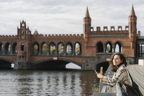 Woman with smartphone in the city at Oberbaum Bridge, Berlin, Germany - AHSF01258