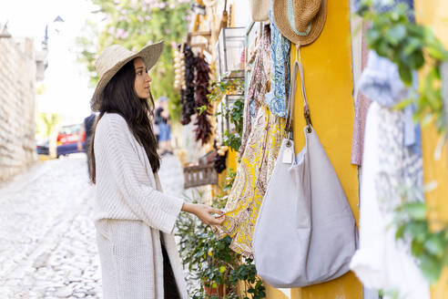 Young woman wearing sun hat and looking on clothes - AFVF04239