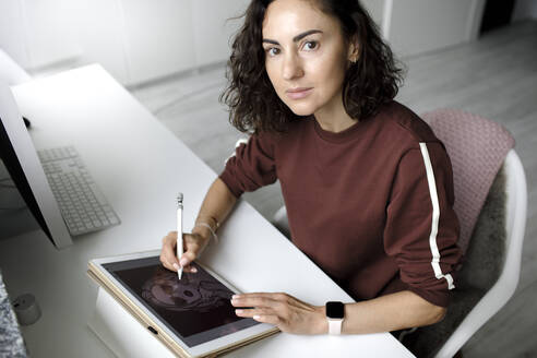 Weibliche Webdesignerin, die zu Hause ein Tablet benutzt und in die Kamera schaut - KMKF01143