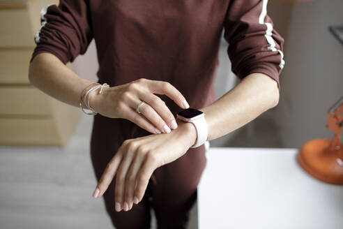 Woman tipping on smart watch at home - KMKF01150