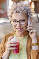 Portrait of a woman using smartphone and drinking a juice outdoors - RTBF01388