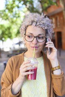 Portrait of a woman using smartphone and drinking a juice outdoors - RTBF01389