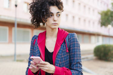 Porträt einer jungen Frau mit Mobiltelefon, die in die Ferne schaut - ERRF02039