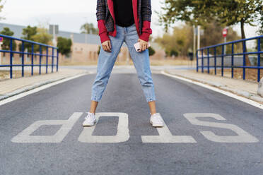 Crop view of young woman with mobile phone standing on the word 'stop' on the street - ERRF02047