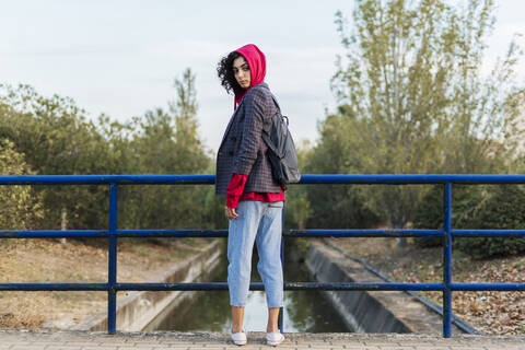 Porträt einer jungen Frau mit Rucksack auf einer Brücke stehend, lizenzfreies Stockfoto