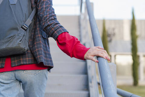 Crop-Ansicht einer jungen Frau mit Rucksack, die eine Treppe hinaufgeht, lizenzfreies Stockfoto