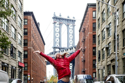 USA, New York, New York City, Young woman jumping against Manhattan Bridge - OCMF00906