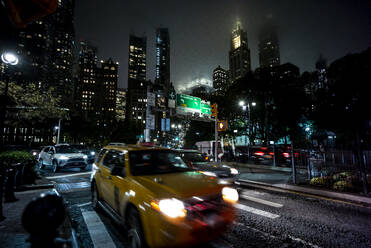 USA, New York, New York City, Verkehr auf der Straße bei Nacht mit hohen Wolkenkratzern im Hintergrund - OCMF00910