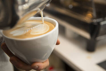 Ausgeschnittenes Bild von Händen, die ein Muster mit Sahne auf Kaffee machen - CAVF69199