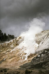 Smoke emitting from volcanic landscape against cloudy sky - CAVF69202