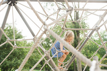 Girl climbing jungle gym in playground - CAVF69204