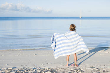 Rückansicht eines Mädchens mit Handtuch am Strand - CAVF69206