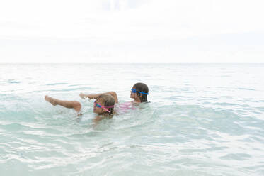 Happy sisters swimming in sea against sky - CAVF69207