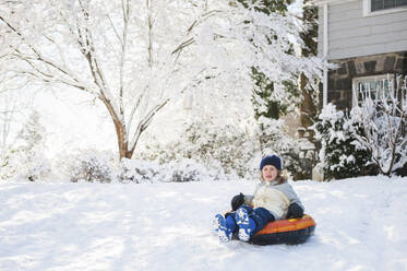 Happy girl sitting on inflatable ring in backyard during winter - CAVF69209