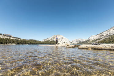 Woman standing at lakeshore against clear blue sky - CAVF69215