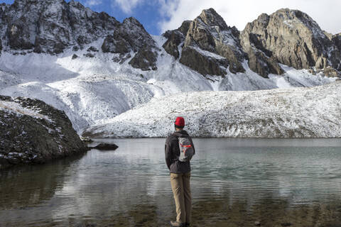 Rückansicht eines Wanderers, der am Seeufer am Berg steht, lizenzfreies Stockfoto