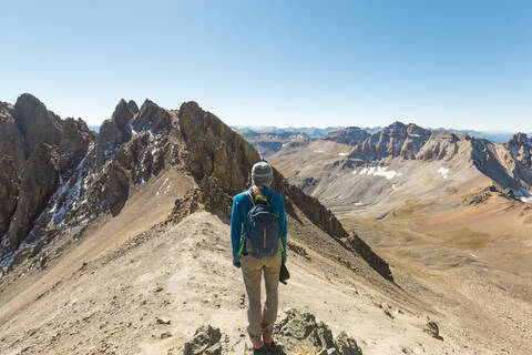 Rückansicht einer Frau, die auf dem Gipfel eines Berges steht, gegen einen klaren blauen Himmel, lizenzfreies Stockfoto