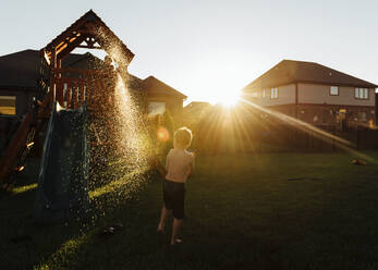 Verspielter Junge bespritzt seinen Bruder mit Wasser, während er auf der Rutsche im Garten steht - CAVF69238