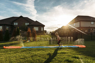 Boy jumping on water slide at backyard - CAVF69244