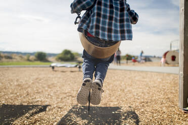 Low section of boy swinging on swing at park - CAVF69257