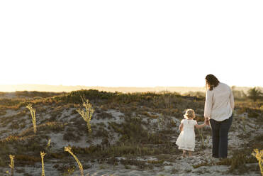 Rear view of mother and daughter holding hands while walking on field - CAVF69267