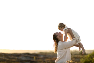 Side view of mother playing with daughter while standing against clear sky - CAVF69268