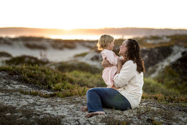 Seitenansicht einer Mutter, die mit ihrer Tochter spielt, während sie im Sand sitzt - CAVF69274