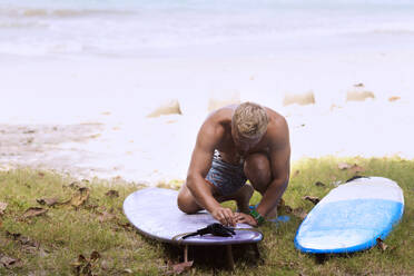 Mann bereitet sich auf Surfboarding vor, während er auf dem Feld hockt - CAVF69283