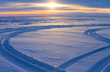 Tire tracks on snow covered field at sunset - CAVF69341