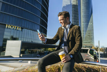 Happy businessman using smartphone in urban business district, Madrid, Spain - KIJF02752