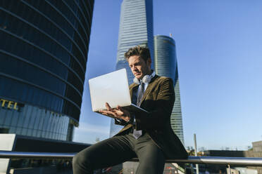 Businessman sitting in urban business district using laptop, Madrid, Spain - KIJF02754